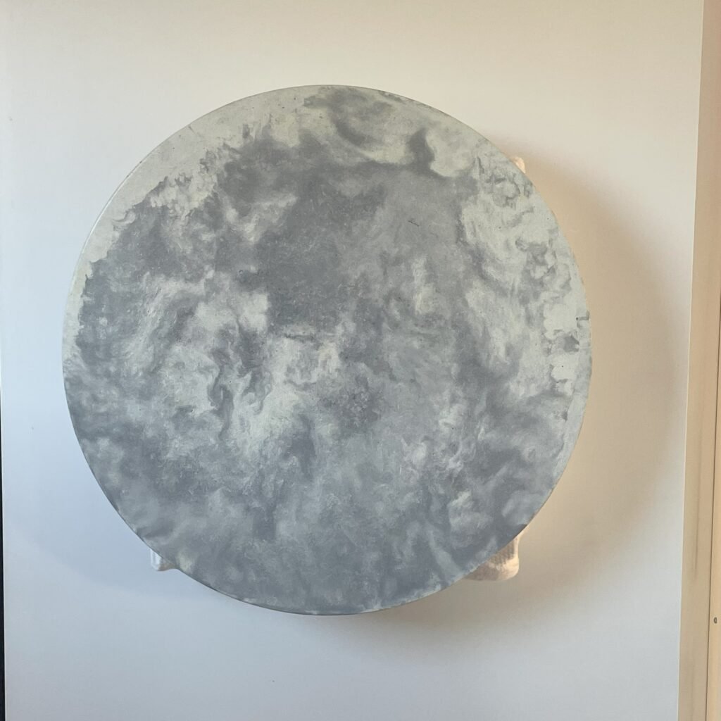 A round, wall-mounted towel warmer in a light faux marble finish, featuring a smooth circular surface with two side-mounted towel hooks. The minimalist design includes a rear compartment for rolled towel storage and a subtle side switch for temperature control. Perfect for modern or spa-inspired bathroom interiors.